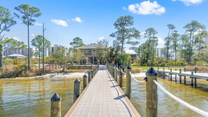 A wooden boardwalk leading to a building with a balcony, surrounded by trees and water. - Cotton Bayou Fish Camp (Orange Beach)