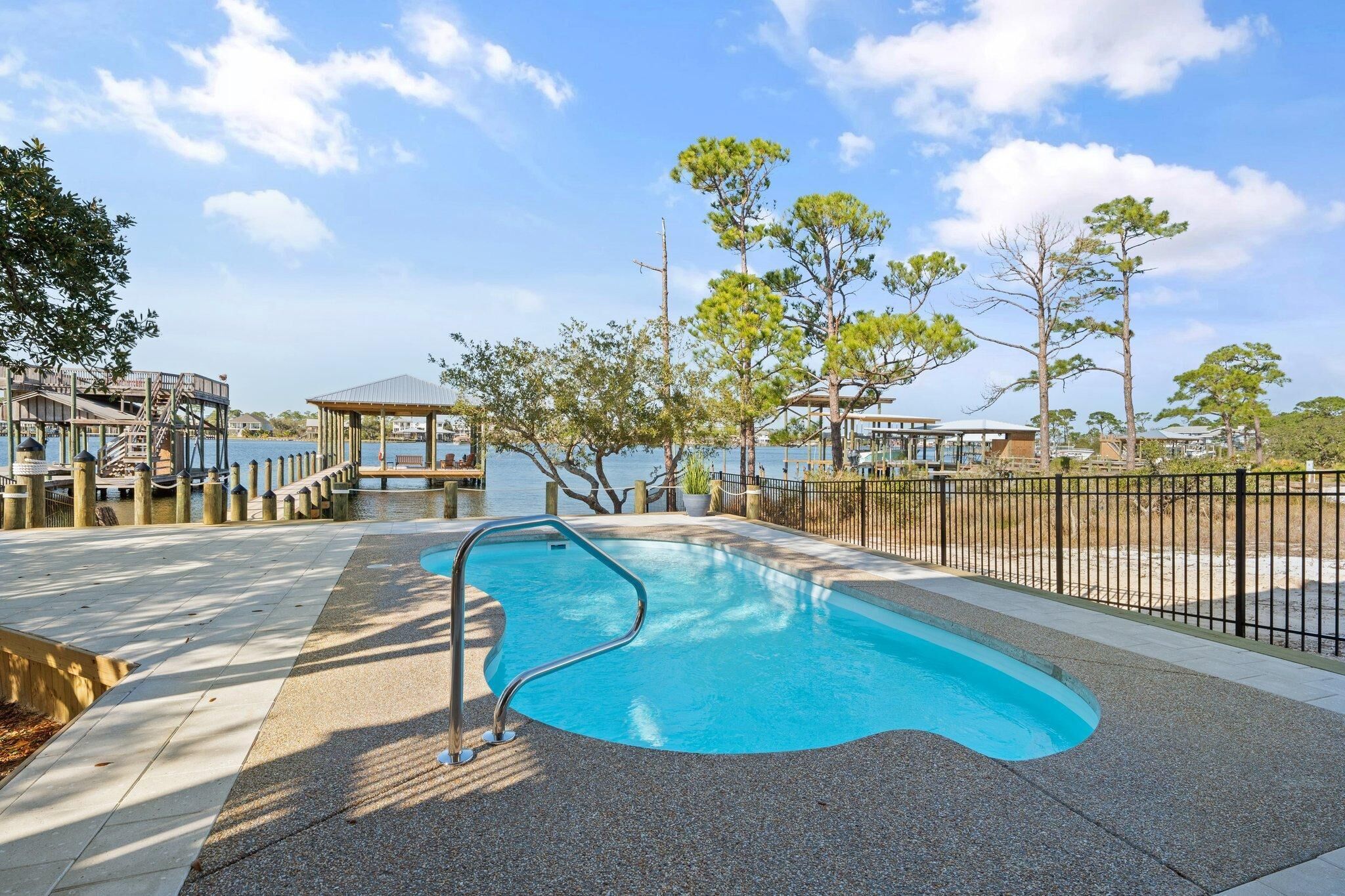 A swimming pool with a metal ladder, surrounded by a paved walkway and a black fence.