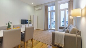 Un salon moderne comprenant un canapé, une table à manger avec des chaises, un téléviseur et une grande fenêtre avec des rideaux.