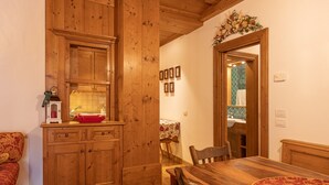 A wooden dining area with a table and chairs, a wooden cabinet with a mirror, and a small red lantern on the counter. - Casa Ciclamino, in the center of Cortina d'Ampezzo (Cortina d´Ampezzo)