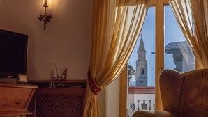 A hotel room with a bed, a TV, a window with curtains, and a view of a building. - Casa Ciclamino, in the center of Cortina d'Ampezzo (Cortina d´Ampezzo)