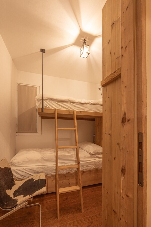 A small, compact room with a bunk bed, a wooden ladder, a small desk, and a wooden wardrobe.