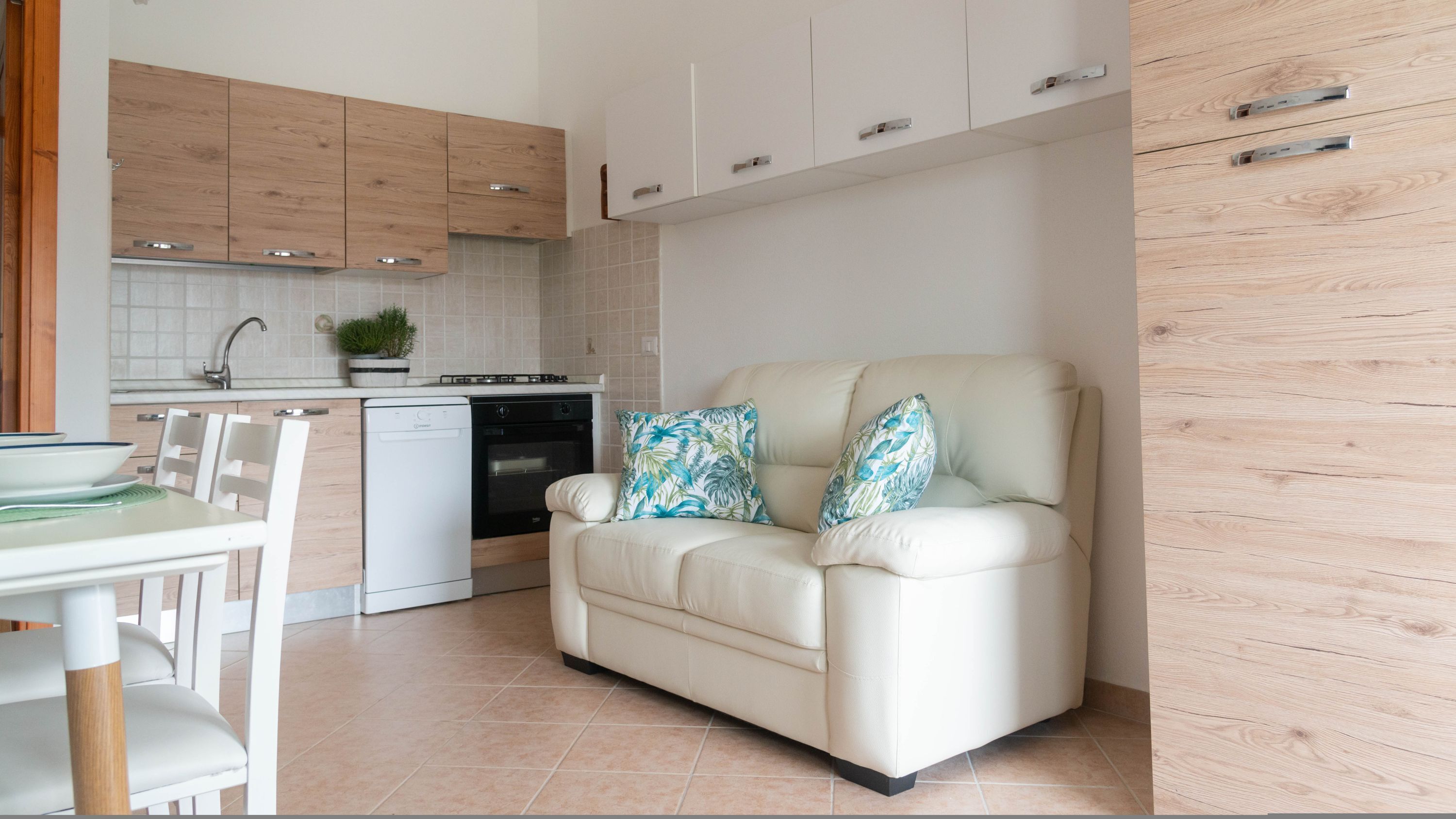 Een moderne keuken met een eethoek, een bank met opvallende kussens en een houten kast.