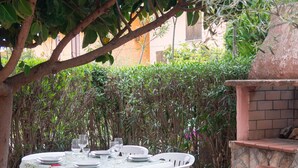 An outdoor dining area with a stone-tiled floor, white plastic chairs, and a table set for four. - Casa Ficus in Porto Ottiolu (Budoni)
