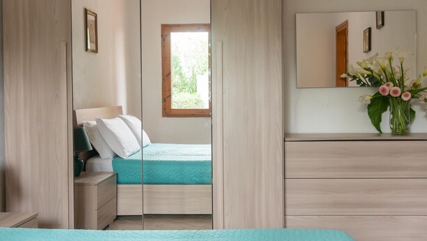 A bedroom with a bed, a dresser, a nightstand, a window, and a mirror. - Casa Ficus in Porto Ottiolu (Budoni)