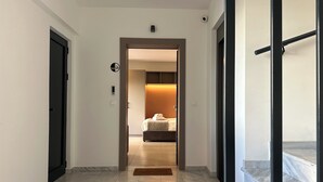 Ein Flur, der zu einem Schlafzimmer führt, mit einem Bett, einem Nachttisch und einem Beistelltisch. Eine Tür ist links und eine Treppe rechts zu sehen.