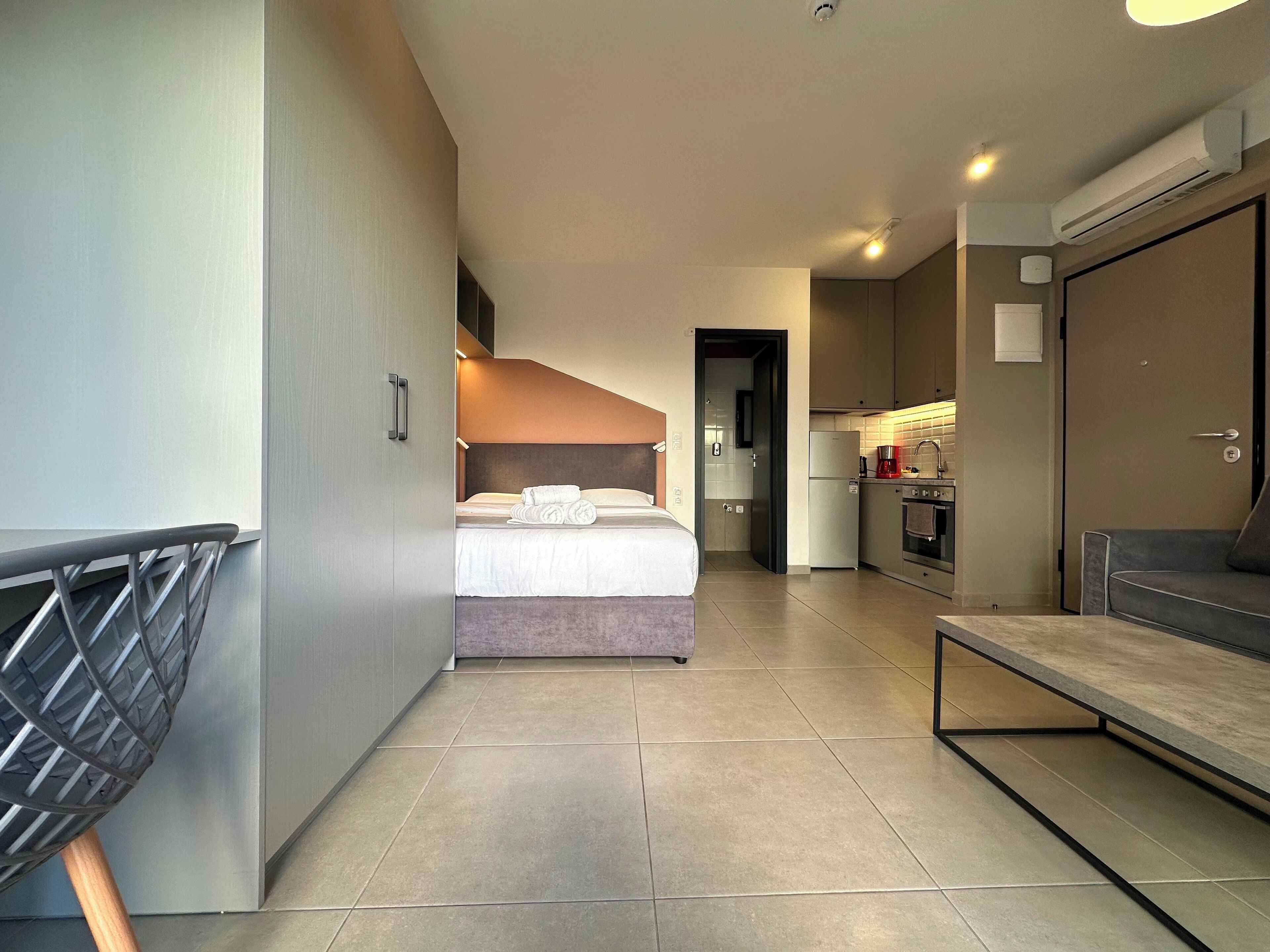 A modern hotel room with a bed, kitchenette, and seating area.