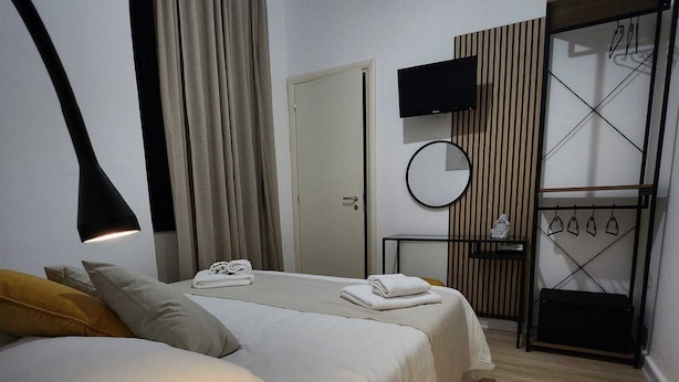 Une chambre d’hôtel avec un lit, une table de chevet, une télévision, un miroir et un mur recouvert de panneaux en bois.