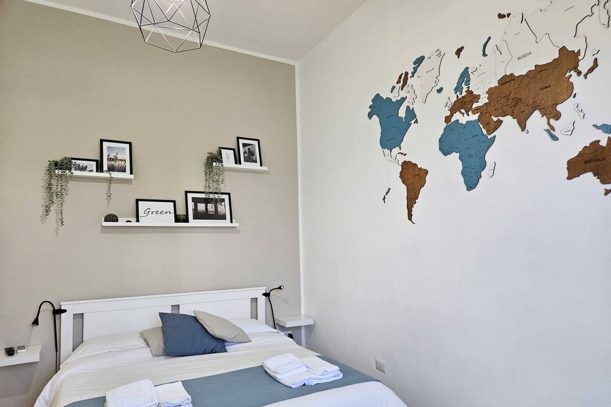 A bedroom with a bed, a world map on the wall, and framed pictures on shelves.