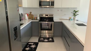 Cocina compacta con gabinetes blancos, un refrigerador de acero inoxidable, microondas, horno y pileta. Hay dos individuales en el suelo.