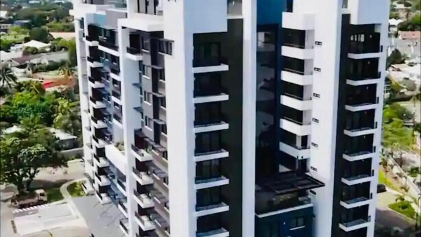 Un moderno edificio residencial de varios pisos, con balcones, un patio central y vistas del paisaje circundante.