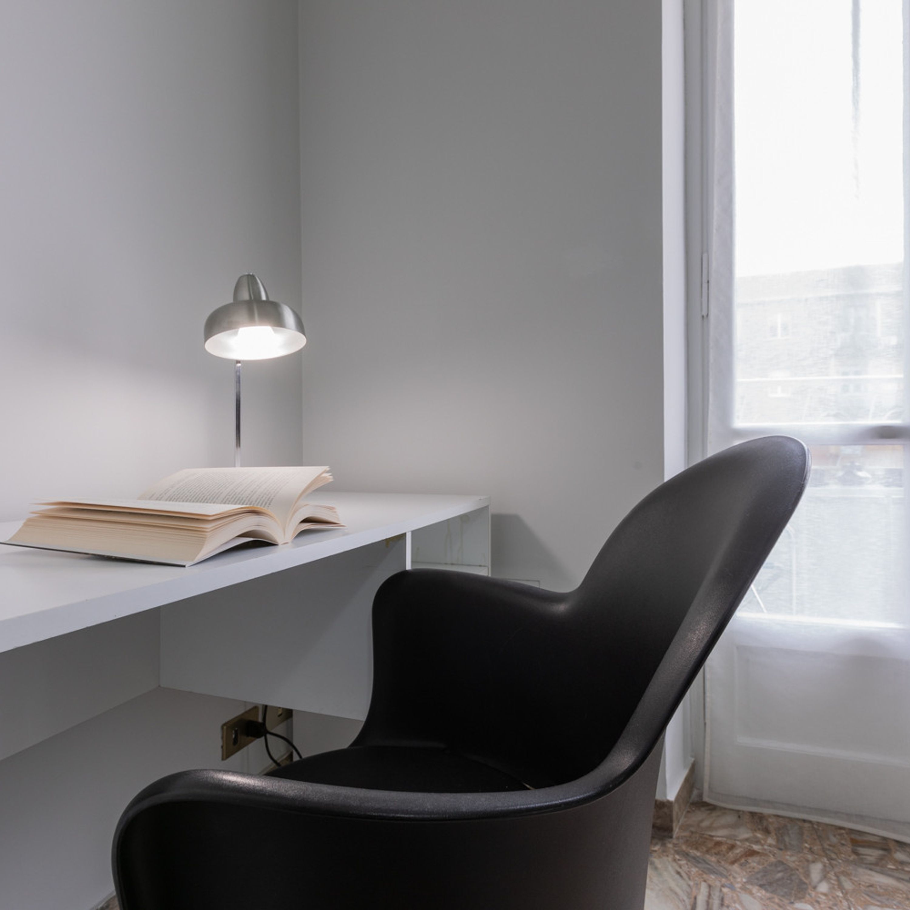 Un espace de travail moderne avec un bureau blanc, une chaise noire et une lampe de bureau.