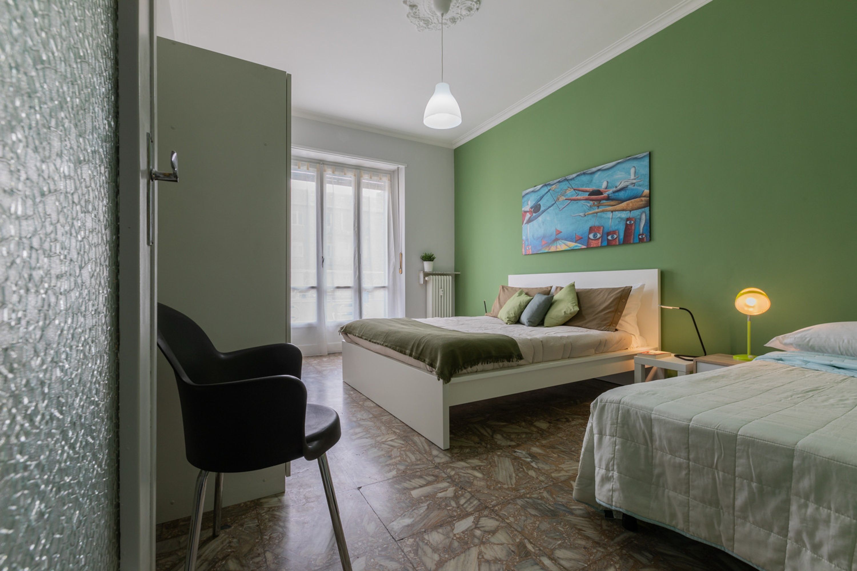 A bedroom with a bed, a chair, a bedside table, a lamp, and a painting on the wall.