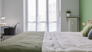 Ett sovrum med en säng, ett skrivbord, en stol, ett element och ett fönster med gardiner.