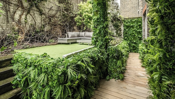 Ein Garten mit einer Holzterrasse, einem Rasen und einer Couch.