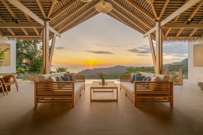 A spacious outdoor seating area with wooden furniture and a view of the sunset over a hilly landscape. - Luxury Jungle Haven ~ Ocean View ~ Infinity Pool! (Dominical)