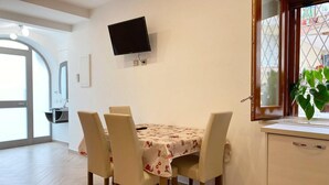 A dining area with a table set for four, a television mounted on the wall, and a window with a view of greenery. - Modern and Cozy Home at 200 Meters to the Beach (Minori)