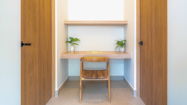 Une pièce d’angle avec un bureau en bois, deux plantes en pot et une chaise.