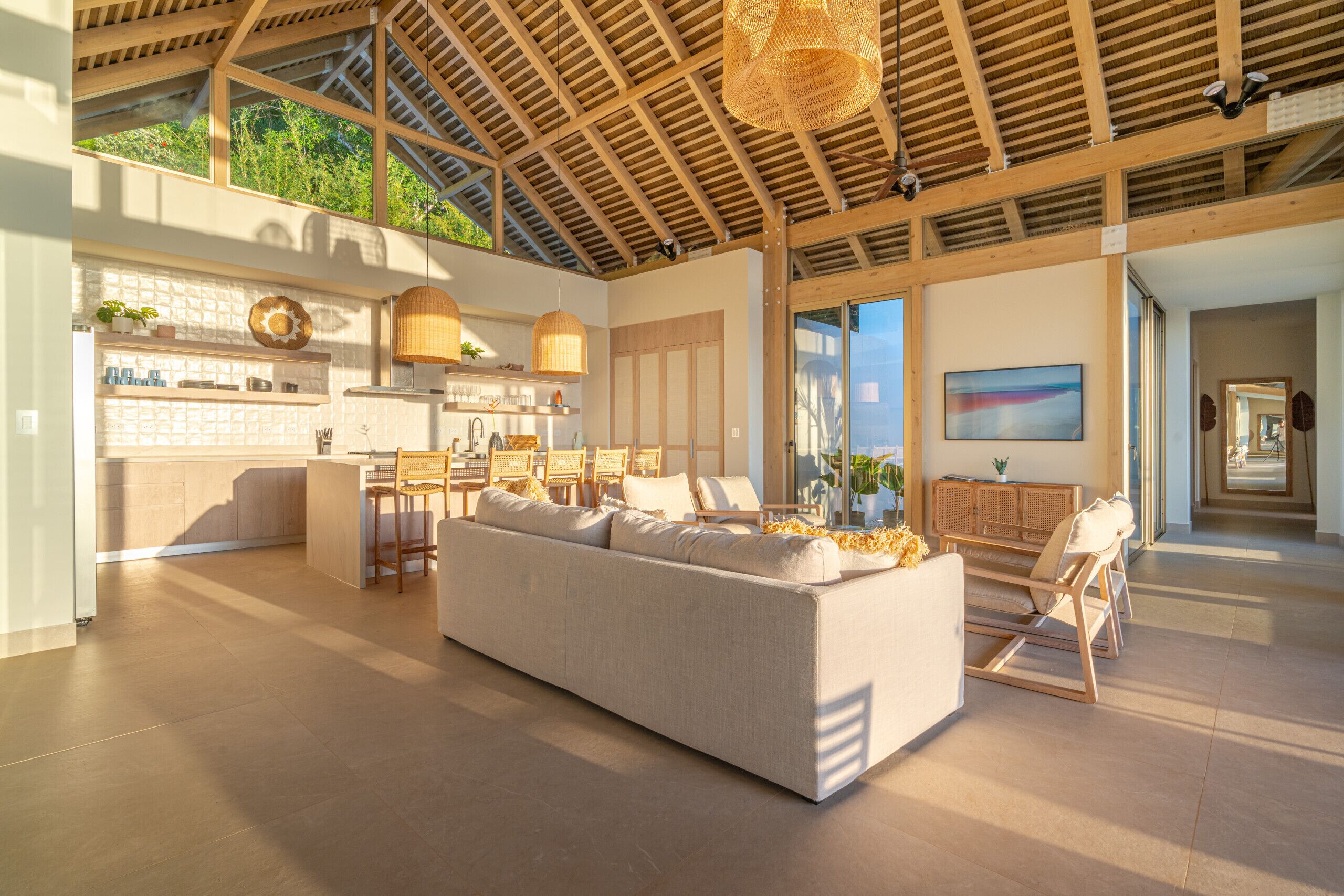 A spacious living area with a large sofa, a kitchen area with a bar, and a dining space with chairs.