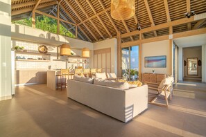 Un grand espace de vie comprenant un grand canapé, un coin cuisine avec un bar et un espace repas avec des chaises.