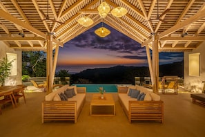 A cozy outdoor seating area with wooden furniture and a view of the sunset over the hills.
