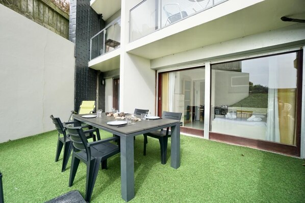 Un coin repas avec une table dressée pour quatre personnes, entourée de chaises, dans un bâtiment moderne doté d’une porte vitrée donnant sur un balcon.