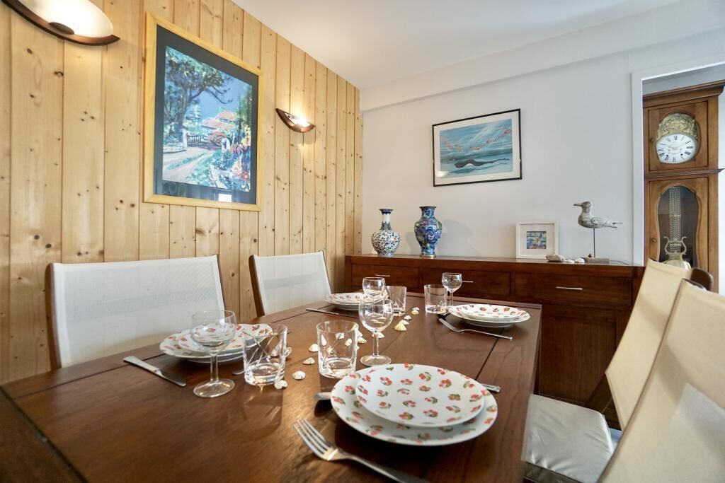 A dining area with a wooden table set for four, surrounded by white chairs.