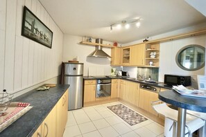 Une cuisine moderne dotée d’appareils électroménagers en acier inoxydable, de meubles de rangement en bois et d’une fenêtre ronde.