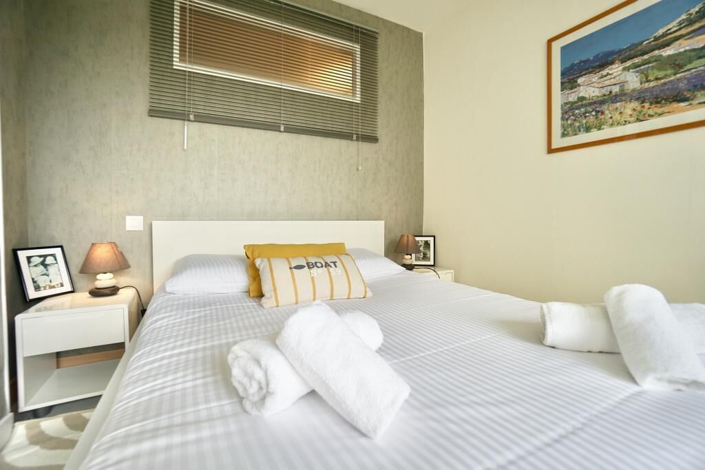 Une chambre d’hôtel avec un lit, une table de chevet, une lampe, un tableau encadré et une fenêtre avec des stores.