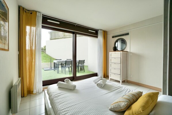 A hotel room with a bed, a dresser, a mirror, and a view of an outdoor area with a table and chairs.