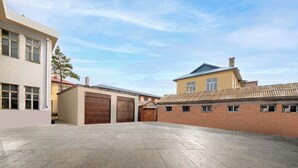 A spacious courtyard with a paved floor, a brick building, and a modern building with large windows and a flat roof. - Binpeng Tianxia Hotel (Harbin)