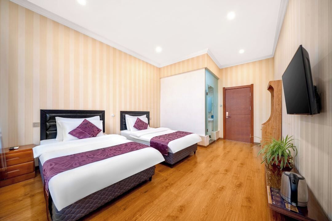 A hotel room with two beds, wooden flooring, a flat-screen TV, and a potted plant.