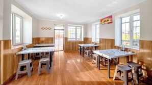 A room with wooden flooring, multiple tables with stools, and large windows providing natural light. - Binpeng Tianxia Hotel (Harbin)