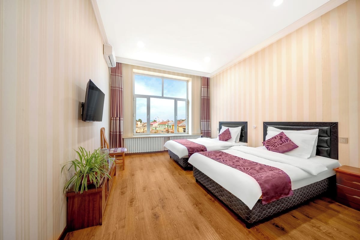 Ein Hotelzimmer mit zwei Betten, einem Fernseher, einem Fenster mit Blick auf die Stadt und einer Zimmerpflanze.
