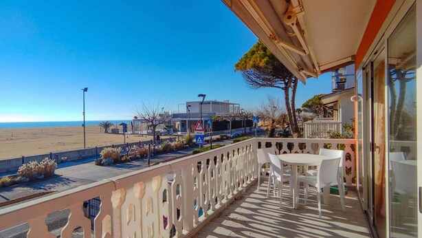 A balcony with a view of the beach, a table and chairs, and a building in the background. - Holiday apartment mit Klimaanlage und Balkon (San Michele al Tagliamento)