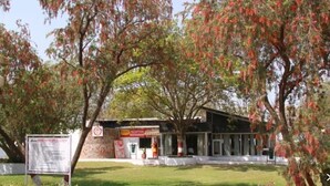 A reception building with a signboard, surrounded by trees with red leaves. - Bird Sanctuary (Gurugram)