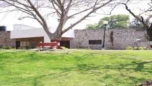 A building with a stone facade, a red bench in front, and a tree providing shade. - Bird Sanctuary (Gurugram)