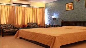 A hotel room with a large bed, two chairs, a small table, and a nightstand. - Bird Sanctuary (Gurugram)