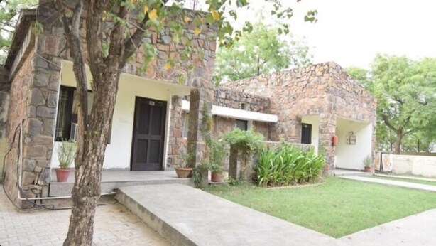 A stone building with a flat roof, a front door, and a small front yard with potted plants. - Bird Sanctuary (Gurugram)