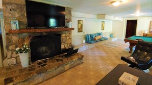 Una sala de estar con chimenea de piedra, televisor de pantalla plana, mesa de billar y un área de estar acogedora.