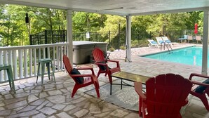 Un patio cubierto con piscina, suelo de piedra y sillas Adirondack rojas.