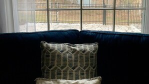 Una habitación con un ventanal grande, un sofá azul y un cojín estampado.