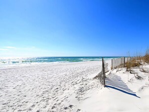 Een zanderig strand met een houten omheining en schaarse begroeiing.