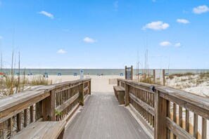 A wooden boardwalk leading to a sandy beach with umbrellas and signs.