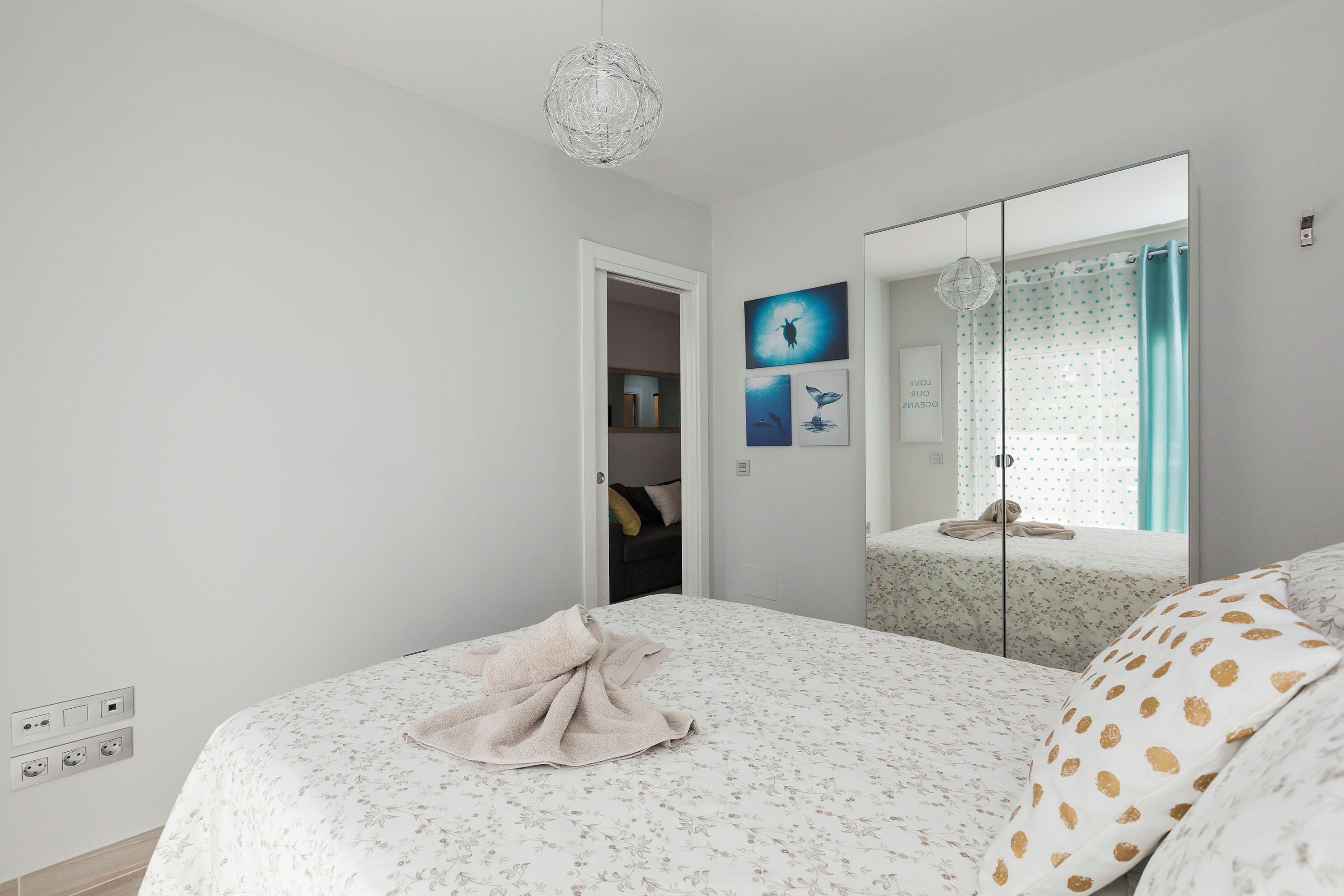 A bedroom with a bed, a mirror, a window with curtains, and a door leading to a bathroom.