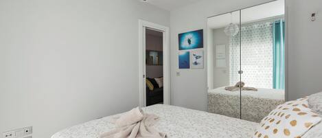 A bedroom with a bed, a mirror, a window with curtains, and a door leading to a bathroom.