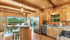 A wooden cabin kitchen with a large island, stainless steel appliances, and a view of a green landscape through the window. - 4 Mi to Sapphire Ski! Mtn-View Cabin w/ Deck (Sapphire)
