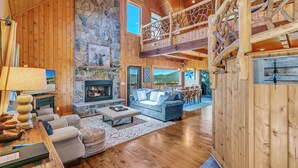 A spacious living room with a stone fireplace, wooden floors, a blue sofa, and a high wooden ceiling with a balcony. - 4 Mi to Sapphire Ski! Mtn-View Cabin w/ Deck (Sapphire)