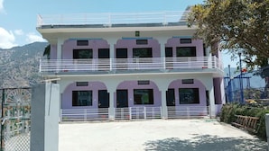 A two-story building with a balcony on the upper floor, a gate on the ground floor, and a mountainous backdrop.