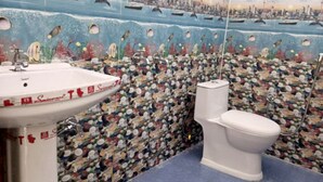 A bathroom with a mosaic tile wall depicting an underwater scene, a white sink, and a toilet.